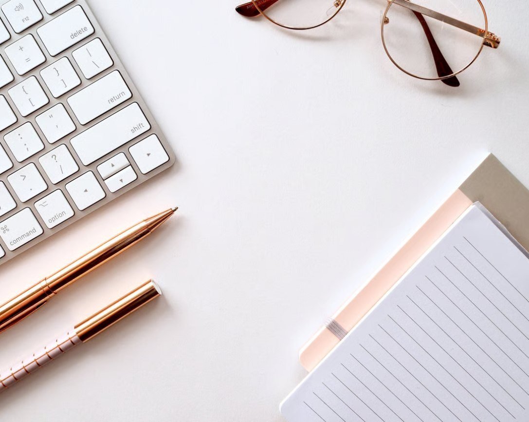 Keyboard, glasses, pens and a notebook on a white desk