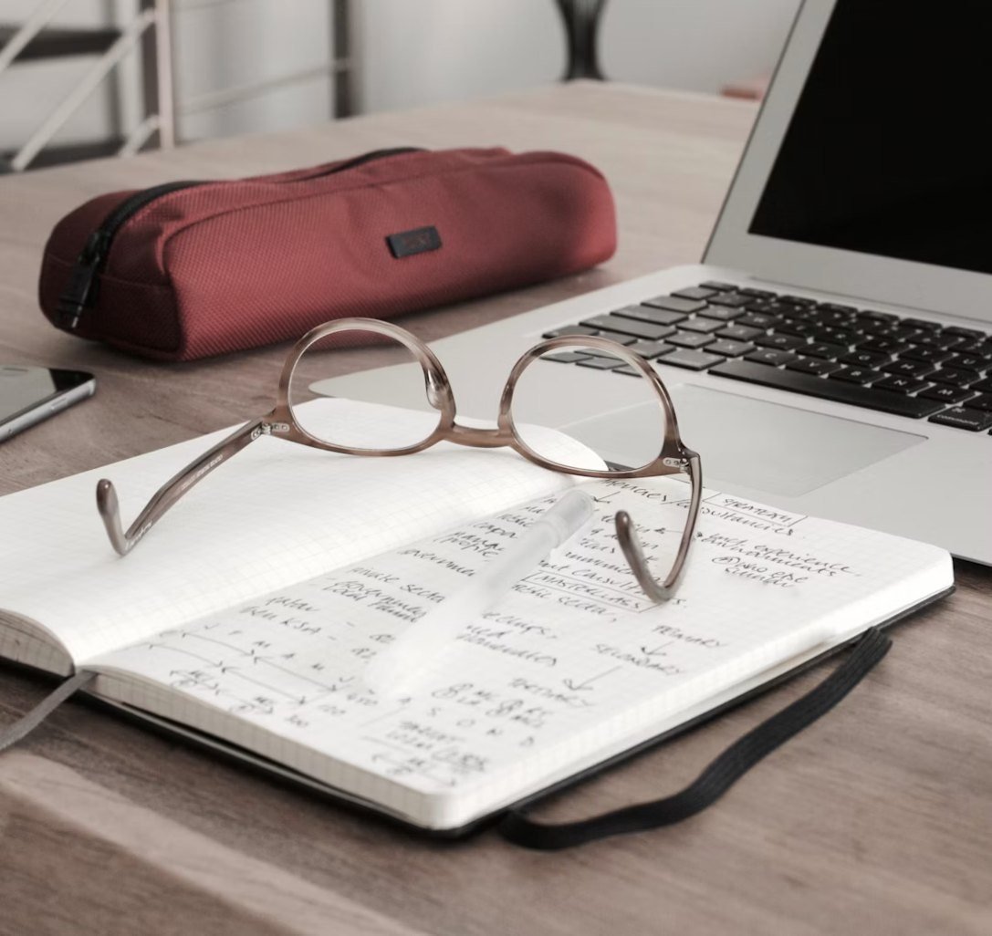 Glasses resting on an open notebook beside a laptop